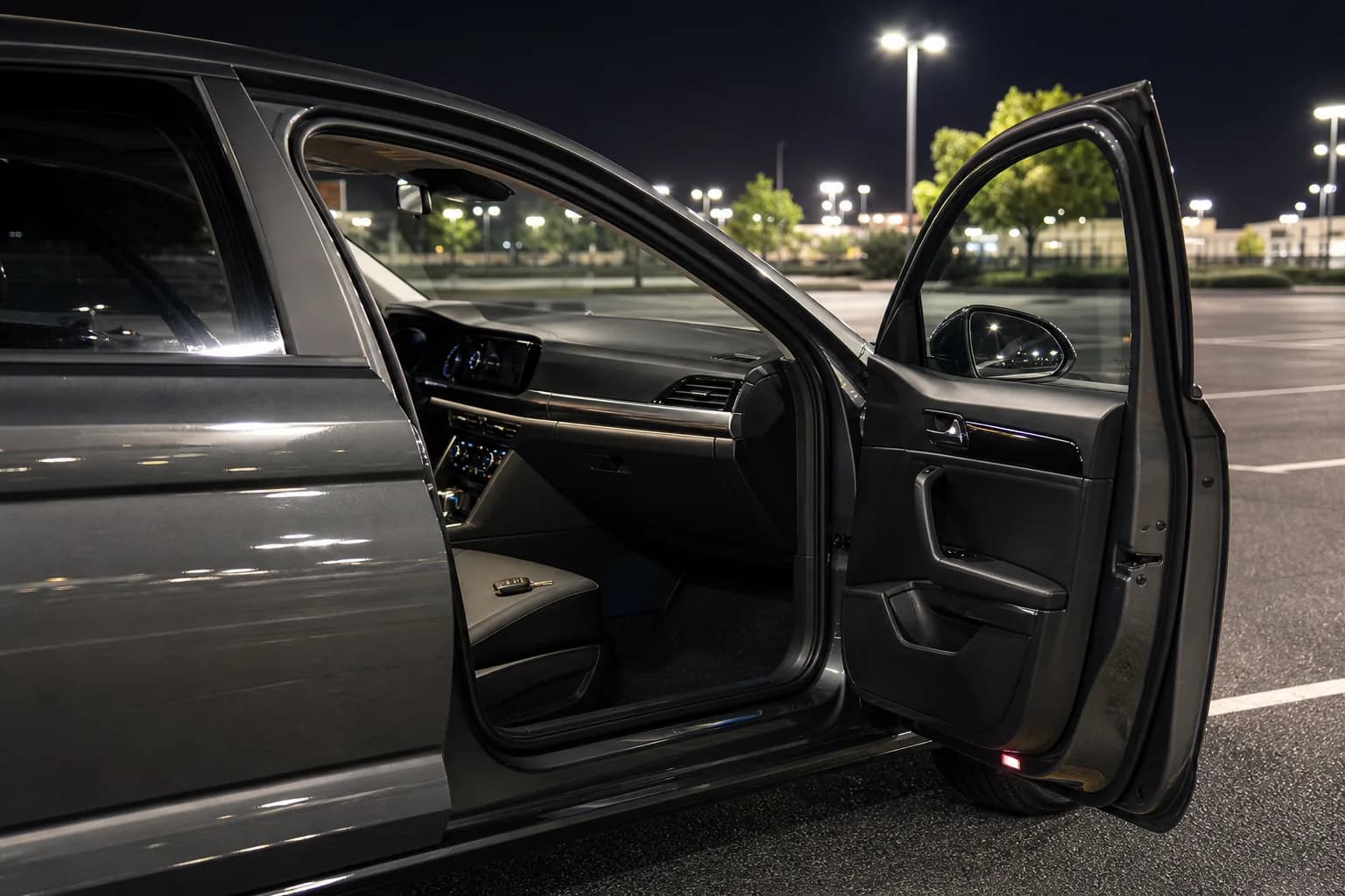 Open car door with keys on the seat on a quiet night lot